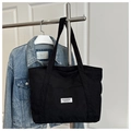 Detalle de bolso tote de pana negra con etiqueta Fashion Instinct en soporte metálico - Negro