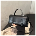 Detailed close-up of a black leather handbag with round buckle and crossbody strap - Black