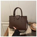 Detail of dark brown leather tote bag with pebble texture and gold hardware on glass table - Brown