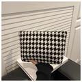 Close-up of black and white houndstooth textured clutch bag held by a person - Black