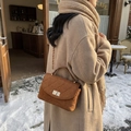 Brown quilted suede handbag with gold lock and chain strap against a winter cafe background - Brown