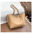 Detailansicht der beigen Ledertasche mit Goldlogo und langen Trägern auf einem Holzboden - Khaki
