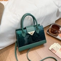 Dark green faux snakeskin leather tote bag with metallic triangle clasp on a bed - Green