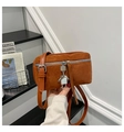Detail van een bruine suède crossbodytas met zilveren rits en robotvormige hanger - Bruin