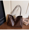 Detail of dark brown tote bag with leather texture leaning against a white door - Brown