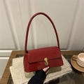 Red patent leather baguette bag with gold metal buckle on beige knit background - Red
