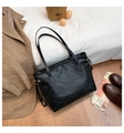 Flat lay of black tote bag with embossed cat patterns on white bedding and wood floor - Black