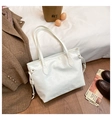 Detail of white embossed tote bag with cat silhouettes on bed with casual accessories - White