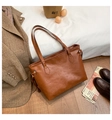Top-down view of a brown embossed tote bag with cartoon patterns on soft white bedding - Brown