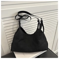 Detalle de bolso hobo de ante negro con correa ajustable y hebilla plateada sobre libros - Negro
