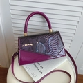 Elegant purple crossbody bag with snake texture flap and glossy finish on display stand - Purple