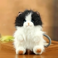 Cute black and white plush cat keychain with fluffy fur and blue eyes on a wood tray - Black