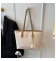 Detail of cream tote bag with brown straps and cute elephant leather charm hanging on wall - White