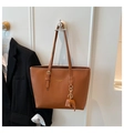 Detailed view of brown tote bag with leather texture, gold logo, and elephant charm - Brown