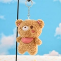 Dettaglio di un portachiavi orsetto di peluche marrone con bavaglino a scacchi rossi su supporto - Orso