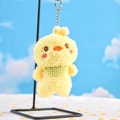 Close-up of yellow plush chick keychain with green plaid scarf on a metal display stand - Chicken