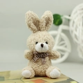 Detailed view of cream plush bunny toy with a brown checkered bow on an artistic base - Tan / 10cm