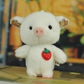 White plush pig keychain with strawberry charm and glitter ears sitting on a book - About 10cm High / White