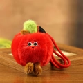 Ciondolo a mela in peluche con viso ricamato e laccio rosso su sfondo in legno naturale - Mela