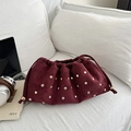 Retro burgundy pleated bucket bag with gold studs on white sofa lifestyle scene - Red