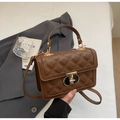 Detail of dark brown quilted crossbody bag with gold-tone metal lock on white bedding - Coffee