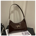 Detail of dark brown patent leather handbag with gold bow buckle on a fashion magazine - Brown