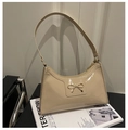 Detalle de bolso de charol beige brillante con cierre de lazo dorado sobre revista - Caqui