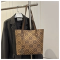 Macro detail of brown tote bag featuring M-letter pattern and golden metal pendant - Brown