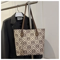 Detail of monogram tote bag with brown straps and gold charm on a black blazer - Khaki