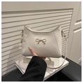 Close-up of textured beige shoulder bag featuring a gold-tone metal bow clasp detail - White