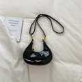 Flat lay of a black patent leather crescent bag with gold zipper on a white fabric background - Black