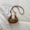 Close-up of brown patent leather crescent bag with gold clasp and elegant logo - Brown