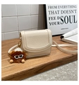 Beige pebble leather crossbody bag with a cute monster charm on a wooden table - With Charm / White