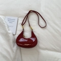 Detail of burgundy patent leather crescent bag with glossy finish and gold metal hardware - Red