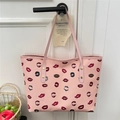 Pink tote bag with vibrant red lip prints and slim handles hanging on a door handle - Pink