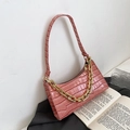 Pink faux crocodile leather underarm bag with gold chain strap on an open book - Pink