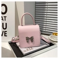 Detalle de bolso pequeño de cuero rosa con hebilla de lazo plateado sobre libros - Rosa