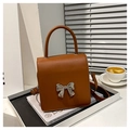 Detail of a brown leather shoulder bag with a silver metallic bow buckle on the cover - Brown