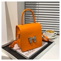 Detalle del bolso naranja de piel con hebilla de lazo plateada en fondo blanco - Naranja
