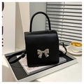 Detalle de un bolso bandolera cuadrado negro con lazo plateado y asa superior - Negro
