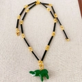 Bamboo chain necklace with green enamel elephant pendant on textured fabric background - Black Chain + Green Elephant