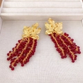 Close-up of gold leaf grape earrings with red beaded tassels on a beige jewelry box - Garnet Red Grape