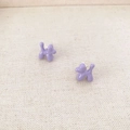 Detail of purple balloon dog stud earrings with enamel finish on beige fabric texture - Purple