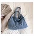 Detail of light blue denim tote bag with square pockets on white textured background - Blue