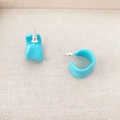 Macro detail of bright blue irregular C-shaped enamel earrings on soft beige fabric - Blue