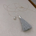 Elegante silberne Tropfenhalskette mit langer hellgrauer Seidenquaste auf Stoff - Graublau