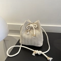 Minimalist straw bucket bag with drawstring closure and bow detail on a black surface - Off White