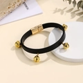 Dettaglio di un bracciale in pelle nera con quattro campanelli dorati e chiusura magnetica - Nero