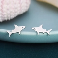 Macro view of polished silver shark earrings displayed on a blue ceramic edge - Shark / Silver