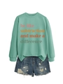 Dettaglio della felpa verde menta con slogan colorato e pantaloncini di jeans strappati - Verde chiaro